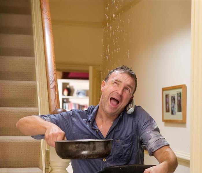 A man holding two pots catching water falling from the ceiling. 
